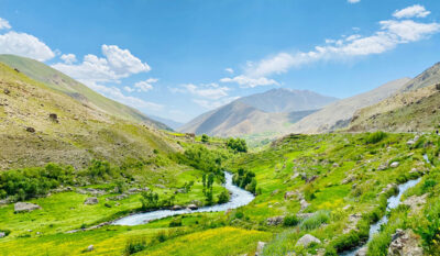 Lush green valley and river in the mountains of Afghanistan under a bright blue sky.