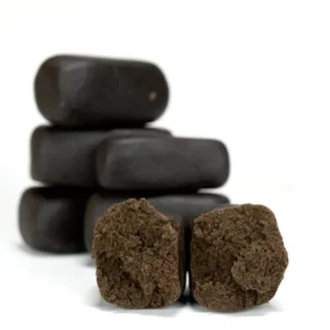 Several dark, hand-pressed hash pieces stacked in the background with two broken open in front to display a soft, resin-rich interior.
